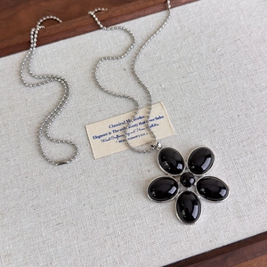 Détail du pendentif fleur en résine noire avec chaîne à billes argentée sur tissu texturé