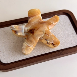 Detail of amber and cream marble acetate starfish hair claw on a wooden tray