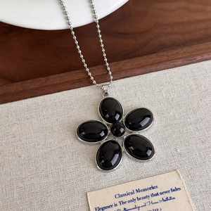 Détail du pendentif fleur en résine noire vintage avec chaîne à billes en argent