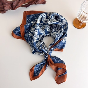 Detail of silk-like paisley square scarf with navy blue pattern and caramel satin border