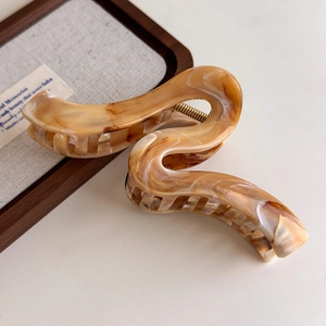 Close-up of an amber marbled resin hair claw clip with S-shaped wavy design on a wooden tray