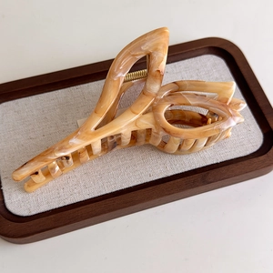 Detailed macro shot of an amber marble tulip hair claw clip on a rustic wooden tray
