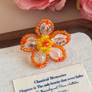Dettaglio di ciondolo a fiore a cinque petali fatto a mano con perle gialle e cristalli arancio