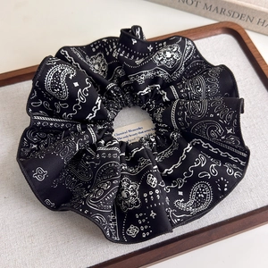 Detail shot of oversized black paisley scrunchie with silk texture in a wooden tray
