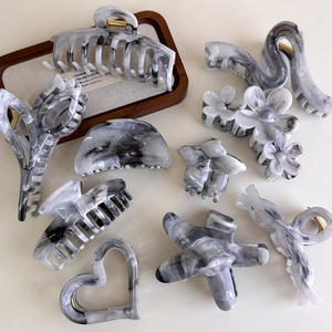 Flat lay of gray marble ink hair claws in star, heart and tulip shapes on beige table