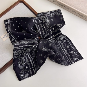Close-up detail of a black paisley silk scarf with classic white patterns and smooth texture
