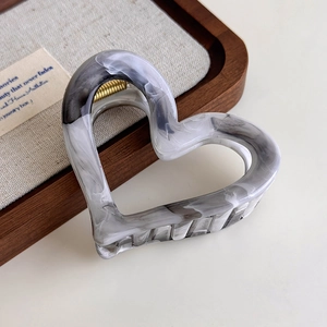Close-up of marble pattern heart hair claw clip with golden metal spring on linen tray