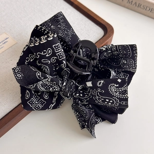 Detail of a black and white Paisley pattern bow hair claw clip on linen background