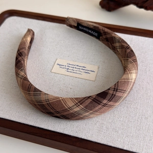 Detail of a brown plaid headband with a handmade label on a soft fabric texture