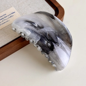 Detail of grey ink-wash marble hair claw clip on a rustic wooden display tray