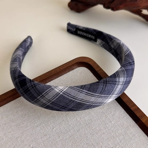 Detail showing grey plaid fabric headband with handmade label on wooden background