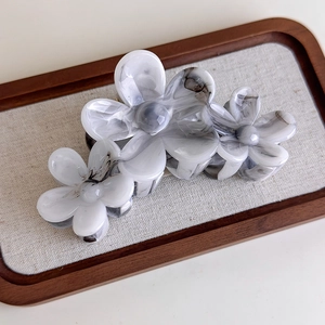 Macro detail of acetate flower hair claw clip with grey marble ink texture on wooden tray