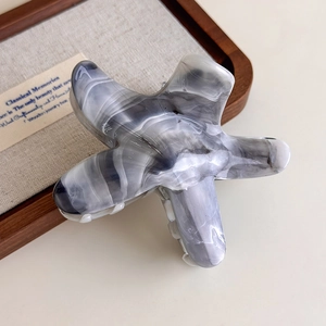 Close-up of starfish acetate hair claw with grey ink marble texture on wooden tray