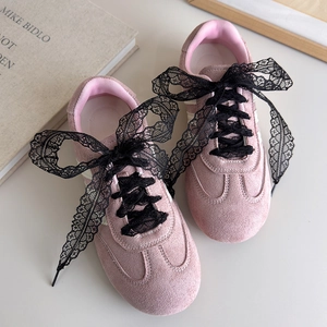 Détail de baskets en daim rose avec de larges lacets en dentelle noire et des bandes