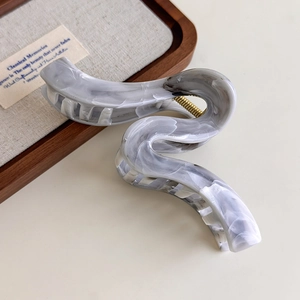 Detail shot of a large wave-shaped hair claw with grey marble ink texture and gold spring