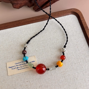 Ethnic beaded necklace with red agate and braided cord on a linen display board