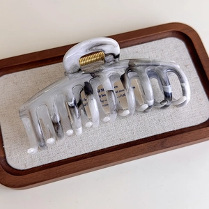 Detail of grey ink marble hair claw clip with golden spring on a wooden tray