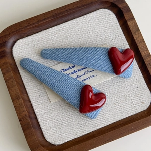 Set of two denim triangle hair clips with red heart accents on a wooden tray