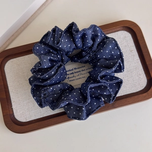 Detailed view of a dark blue polka dot denim scrunchie displayed on a vintage tray