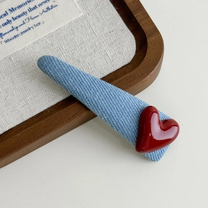 Detail of blue denim fabric hair clip with a glossy red 3D heart on a textured background