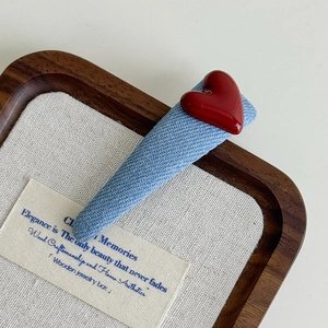 Detail of light blue denim fabric hair clip with a shiny red 3D heart on a wooden tray