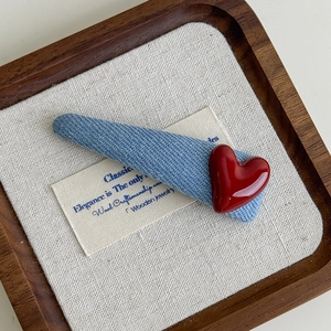 Close-up of blue denim hair clip with a red heart charm on a wooden display tray