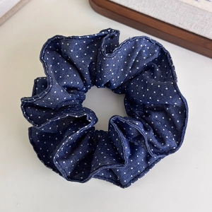 Detailed close-up of a blue polka dot denim scrunchie with layered pleats on white surface