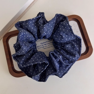 Close-up of dark blue polka dot denim scrunchie with layered pleats on a wooden tray