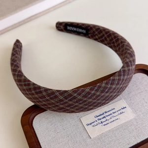 Detailed view of dark brown plaid headband with handmade label on a wooden tray