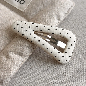 Macro detail of beige fabric polka dot hair clip showing fine texture and inner metal clip