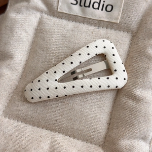 Detailed view of a fabric triangle hair clip with black polka dots on cream background