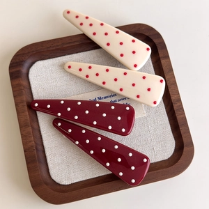 Close-up of four red and white polka dot teardrop hair clips on a linen texture tray