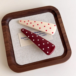 Retro triangle hair clips with red and white polka dots on a wooden tray