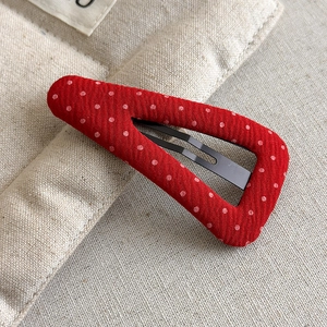 Detailed macro view of a red fabric hair clip with white polka dots and a black metal clip