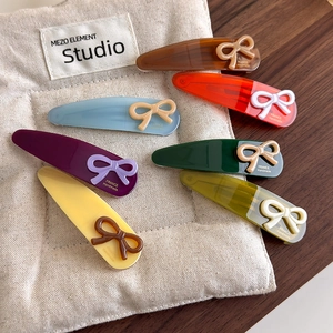 Set of seven colorful resin teardrop hair clips with elegant bow details on a soft fabric pad