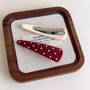 Close-up of red polka dot and cream hair clips on a wooden tray with linen decor