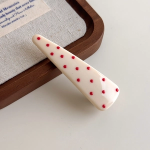 Detail of a creamy white hair clip with red polka dots on a rustic wooden tray and linen