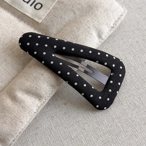 Detailed view of a black fabric BB hair clip with white polka dots on textured linen
