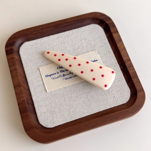 Detail of vintage red polka dot duckbill hair clip on a premium linen and wood display