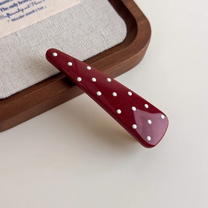 Close-up of a burgundy teardrop hair clip with white polka dots and golden glitter finish