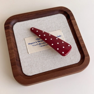 Close-up of a vintage red polka dot hair clip on a minimalist wooden display tray