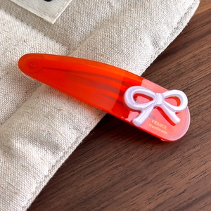 Close-up of handmade orange acetate bow hair clip with gold France lettering on fabric