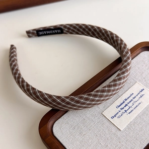 Close-up of brown plaid headband featuring a stitched handmade label and retro style