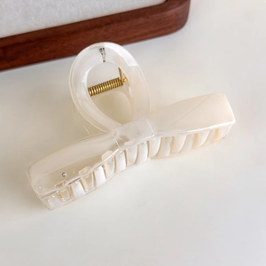 Detail of a large cream hair claw clip with golden spring on marble background