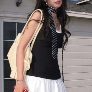 Detail of preppy black vest with lace trim, pleated skirt, and striped tie accessory