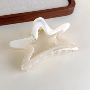 Detail of star-shaped hair claw clip with creamy white gradient and gold spring