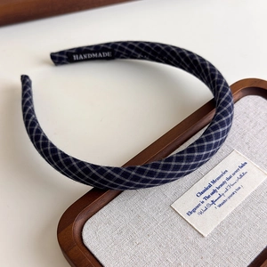 Detail of a navy plaid fabric headband with a handmade label on a walnut display tray