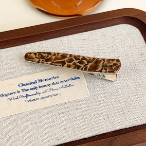 Détail d'une pince à cheveux vintage en acétate avec motif léopard sur plateau en bois