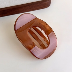 Macro detail of amber brown hollow oval hair claw clip with glossy translucent finish