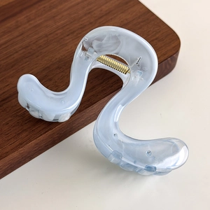 Close-up of S-shaped blue marble acetate hair claw clip with a golden metal spring
